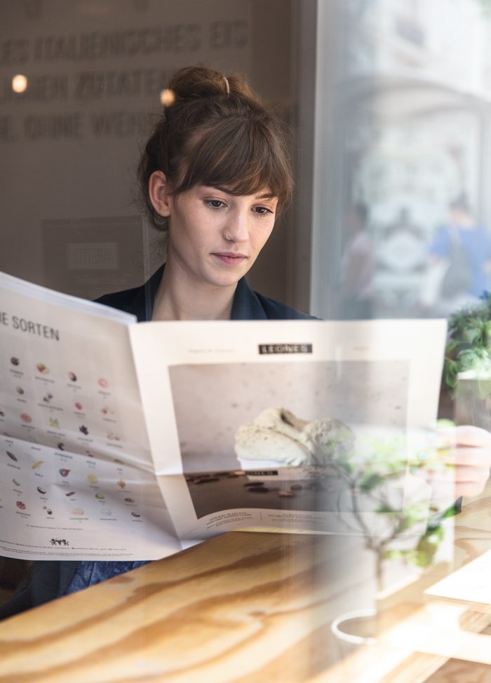 Junge Kundin liest die erste Ausgabe der Leones Zeitung im Eissalon